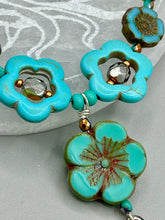 Load image into Gallery viewer, Adorn your look and show your affinity for nature with this exquisite handcrafted necklace, composed of a large intricate sea-green hibiscus pressed glass bead, a lucky hand charm, multiple turquoise, and dark avocado green faceted pressed glass beads, and a hook-eye clasp for secure wear. This nature-inspired statement piece brings warmth to any outfit for both day and night. Measurements:  Necklace: 19 1/2&quot;, Flower and lucky hand pendant 3&quot;
