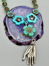 Load image into Gallery viewer, Adorn your look and show your affinity for nature with this exquisite handcrafted necklace, composed of a large intricate sea-green hibiscus pressed glass bead, a lucky hand charm, multiple turquoise, and dark avocado green faceted pressed glass beads, and a hook-eye clasp for secure wear. This nature-inspired statement piece brings warmth to any outfit for both day and night. Measurements:  Necklace: 19 1/2&quot;, Flower and lucky hand pendant 3&quot;
