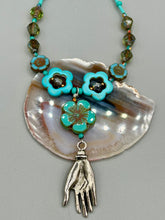 Load image into Gallery viewer, Adorn your look and show your affinity for nature with this exquisite handcrafted necklace, composed of a large intricate sea-green hibiscus pressed glass bead, a lucky hand charm, multiple turquoise, and dark avocado green faceted pressed glass beads, and a hook-eye clasp for secure wear. This nature-inspired statement piece brings warmth to any outfit for both day and night. Measurements:  Necklace: 19 1/2&quot;, Flower and lucky hand pendant 3&quot;
