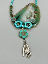 Load image into Gallery viewer, Adorn your look and show your affinity for nature with this exquisite handcrafted necklace, composed of a large intricate sea-green hibiscus pressed glass bead, a lucky hand charm, multiple turquoise, and dark avocado green faceted pressed glass beads, and a hook-eye clasp for secure wear. This nature-inspired statement piece brings warmth to any outfit for both day and night. Measurements:  Necklace: 19 1/2&quot;, Flower and lucky hand pendant 3&quot;
