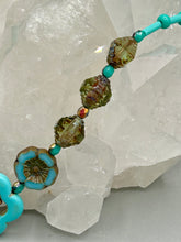 Load image into Gallery viewer, Adorn your look and show your affinity for nature with this exquisite handcrafted necklace, composed of a large intricate sea-green hibiscus pressed glass bead, a lucky hand charm, multiple turquoise, and dark avocado green faceted pressed glass beads, and a hook-eye clasp for secure wear. This nature-inspired statement piece brings warmth to any outfit for both day and night. Measurements:  Necklace: 19 1/2&quot;, Flower and lucky hand pendant 3&quot;
