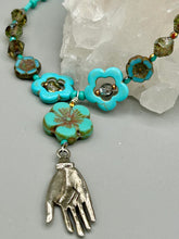 Load image into Gallery viewer, Adorn your look and show your affinity for nature with this exquisite handcrafted necklace, composed of a large intricate sea-green hibiscus pressed glass bead, a lucky hand charm, multiple turquoise, and dark avocado green faceted pressed glass beads, and a hook-eye clasp for secure wear. This nature-inspired statement piece brings warmth to any outfit for both day and night. Measurements:  Necklace: 19 1/2&quot;, Flower and lucky hand pendant 3&quot;
