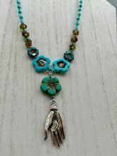 Load image into Gallery viewer, Adorn your look and show your affinity for nature with this exquisite handcrafted necklace, composed of a large intricate sea-green hibiscus pressed glass bead, a lucky hand charm, multiple turquoise, and dark avocado green faceted pressed glass beads, and a hook-eye clasp for secure wear. This nature-inspired statement piece brings warmth to any outfit for both day and night. Measurements:  Necklace: 19 1/2&quot;, Flower and lucky hand pendant 3&quot;
