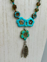 Load image into Gallery viewer, Adorn your look and show your affinity for nature with this exquisite handcrafted necklace, composed of a large intricate sea-green hibiscus pressed glass bead, a lucky hand charm, multiple turquoise, and dark avocado green faceted pressed glass beads, and a hook-eye clasp for secure wear. This nature-inspired statement piece brings warmth to any outfit for both day and night. Measurements:  Necklace: 19 1/2&quot;, Flower and lucky hand pendant 3&quot;
