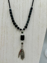 Load image into Gallery viewer, This elegant black obsidian square-shaped beaded necklace is the perfect accessory for your unique look. With a large black bead adorned with multi-color cloisonné bead and a lucky hand charm, it exudes a dark, alluring vibe. Complemented with black glass and hematite stone beads, it will make a bold statement.  Measurements:  Necklace: 18” in length - lucky hand charm is 3 1 /2” Height
