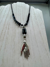 Load image into Gallery viewer, This elegant black obsidian square-shaped beaded necklace is the perfect accessory for your unique look. With a large black bead adorned with multi-color cloisonné bead and a lucky hand charm, it exudes a dark, alluring vibe. Complemented with black glass and hematite stone beads, it will make a bold statement.  Measurements:  Necklace: 18” in length - lucky hand charm is 3 1 /2” Height
