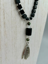 Load image into Gallery viewer, This elegant black obsidian square-shaped beaded necklace is the perfect accessory for your unique look. With a large black bead adorned with multi-color cloisonné bead and a lucky hand charm, it exudes a dark, alluring vibe. Complemented with black glass and hematite stone beads, it will make a bold statement.  Measurements:  Necklace: 18” in length - lucky hand charm is 3 1 /2” Height
