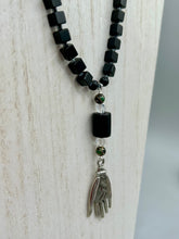 Load image into Gallery viewer, This elegant black obsidian square-shaped beaded necklace is the perfect accessory for your unique look. With a large black bead adorned with multi-color cloisonné bead and a lucky hand charm, it exudes a dark, alluring vibe. Complemented with black glass and hematite stone beads, it will make a bold statement.  Measurements:  Necklace: 18” in length - lucky hand charm is 3 1 /2” Height
