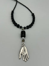 Load image into Gallery viewer, This elegant black obsidian square-shaped beaded necklace is the perfect accessory for your unique look. With a large black bead adorned with multi-color cloisonné bead and a lucky hand charm, it exudes a dark, alluring vibe. Complemented with black glass and hematite stone beads, it will make a bold statement.  Measurements:  Necklace: 18” in length - lucky hand charm is 3 1 /2” Height
