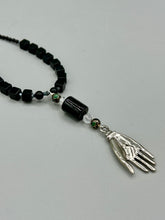Load image into Gallery viewer, This elegant black obsidian square-shaped beaded necklace is the perfect accessory for your unique look. With a large black bead adorned with multi-color cloisonné bead and a lucky hand charm, it exudes a dark, alluring vibe. Complemented with black glass and hematite stone beads, it will make a bold statement.  Measurements:  Necklace: 18” in length - lucky hand charm is 3 1 /2” Height
