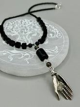 Load image into Gallery viewer, This elegant black obsidian square-shaped beaded necklace is the perfect accessory for your unique look. With a large black bead adorned with multi-color cloisonné bead and a lucky hand charm, it exudes a dark, alluring vibe. Complemented with black glass and hematite stone beads, it will make a bold statement.  Measurements:  Necklace: 18” in length - lucky hand charm is 3 1 /2” Height
