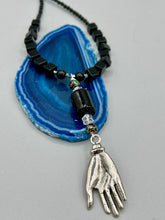 Load image into Gallery viewer, This elegant black obsidian square-shaped beaded necklace is the perfect accessory for your unique look. With a large black bead adorned with multi-color cloisonné bead and a lucky hand charm, it exudes a dark, alluring vibe. Complemented with black glass and hematite stone beads, it will make a bold statement.  Measurements:  Necklace: 18” in length - lucky hand charm is 3 1 /2” Height

