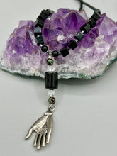 Load image into Gallery viewer, This elegant black obsidian square-shaped beaded necklace is the perfect accessory for your unique look. With a large black bead adorned with multi-color cloisonné bead and a lucky hand charm, it exudes a dark, alluring vibe. Complemented with black glass and hematite stone beads, it will make a bold statement.  Measurements:  Necklace: 18” in length - lucky hand charm is 3 1 /2” Height
