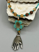 Load image into Gallery viewer, Complete your look with this carefully crafted necklace, featuring a large sea-green hibiscus pressed glass bead, a lucky hand charm, assorted champagne melon beads, and turquoise glass beads. All these elements are combined with a hook-eye clasp, ensuring lasting wear. This nature-inspired accessory adds a touch of charm to all kinds of outfits, making it ideal for both day and night. Measurements:   Necklace: 18&quot;
