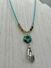 Load image into Gallery viewer, Complete your look with this carefully crafted necklace, featuring a large sea-green hibiscus pressed glass bead, a lucky hand charm, assorted champagne melon beads, and turquoise glass beads. All these elements are combined with a hook-eye clasp, ensuring lasting wear. This nature-inspired accessory adds a touch of charm to all kinds of outfits, making it ideal for both day and night. Measurements:   Necklace: 18&quot;
