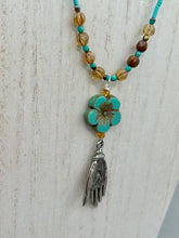 Load image into Gallery viewer, Complete your look with this carefully crafted necklace, featuring a large sea-green hibiscus pressed glass bead, a lucky hand charm, assorted champagne melon beads, and turquoise glass beads. All these elements are combined with a hook-eye clasp, ensuring lasting wear. This nature-inspired accessory adds a touch of charm to all kinds of outfits, making it ideal for both day and night. Measurements:   Necklace: 18&quot;
