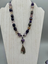Load image into Gallery viewer, This nature-inspired accessory features an array of unique hues, including rainbow fluorite stone beads and iridescent dark shimmery purple glass beads with hints of gold, blue, pink, and green. The secure hook-eye clasp makes it perfect for day to night wear, allowing you to add a touch of summer to your wardrobe. The necklace is further complemented by a large square-shaped rainbow fluorite bead and a lucky hand charm. Measurements:  Necklace: 18&quot;, Lucky hand pendant 3&quot;
