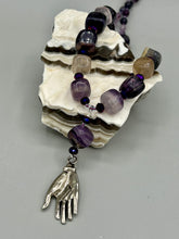 Load image into Gallery viewer, This nature-inspired accessory features an array of unique hues, including rainbow fluorite stone beads and iridescent dark shimmery purple glass beads with hints of gold, blue, pink, and green. The secure hook-eye clasp makes it perfect for day to night wear, allowing you to add a touch of summer to your wardrobe. The necklace is further complemented by a large square-shaped rainbow fluorite bead and a lucky hand charm. Measurements:  Necklace: 18&quot;, Lucky hand pendant 3&quot;
