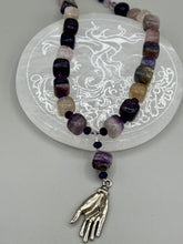Load image into Gallery viewer, This nature-inspired accessory features an array of unique hues, including rainbow fluorite stone beads and iridescent dark shimmery purple glass beads with hints of gold, blue, pink, and green. The secure hook-eye clasp makes it perfect for day to night wear, allowing you to add a touch of summer to your wardrobe. The necklace is further complemented by a large square-shaped rainbow fluorite bead and a lucky hand charm. Measurements:  Necklace: 18&quot;, Lucky hand pendant 3&quot;
