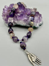 Load image into Gallery viewer, This nature-inspired accessory features an array of unique hues, including rainbow fluorite stone beads and iridescent dark shimmery purple glass beads with hints of gold, blue, pink, and green. The secure hook-eye clasp makes it perfect for day to night wear, allowing you to add a touch of summer to your wardrobe. The necklace is further complemented by a large square-shaped rainbow fluorite bead and a lucky hand charm. Measurements:  Necklace: 18&quot;, Lucky hand pendant 3&quot;
