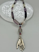 Load image into Gallery viewer, This nature-inspired accessory features an array of unique hues, including rectangular-shaped rainbow fluorite stone beads, round amethyst beads and dark purple glass beads. The secure hook-eye clasp makes it perfect for day to night wear, allowing you to add a touch of summer to your wardrobe. The necklace is further complemented by a large square-shaped rainbow fluorite bead and a lucky hand charm.  Measurements:  Necklace: 18&quot;, Lucky hand pendant 3&quot;
