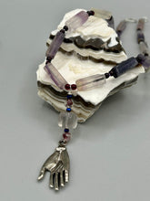 Load image into Gallery viewer, This nature-inspired accessory features an array of unique hues, including rectangular-shaped rainbow fluorite stone beads, round amethyst beads and dark purple glass beads. The secure hook-eye clasp makes it perfect for day to night wear, allowing you to add a touch of summer to your wardrobe. The necklace is further complemented by a large square-shaped rainbow fluorite bead and a lucky hand charm.  Measurements:  Necklace: 18&quot;, Lucky hand pendant 3&quot;
