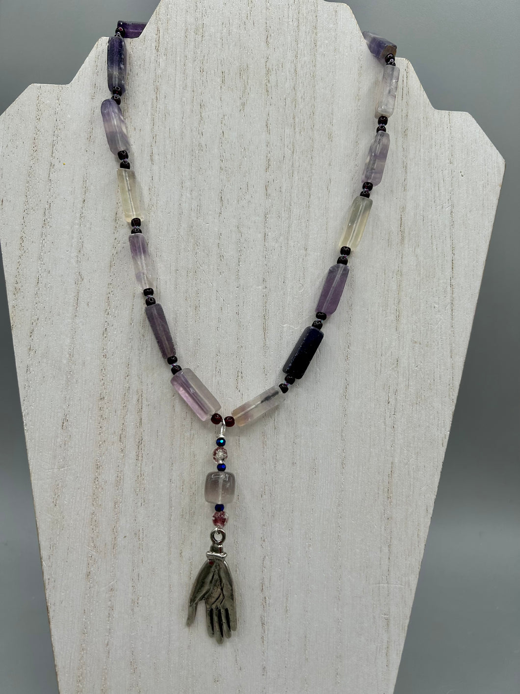 This nature-inspired accessory features an array of unique hues, including rectangular-shaped rainbow fluorite stone beads, round amethyst beads and dark purple glass beads. The secure hook-eye clasp makes it perfect for day to night wear, allowing you to add a touch of summer to your wardrobe. The necklace is further complemented by a large square-shaped rainbow fluorite bead and a lucky hand charm.  Measurements:  Necklace: 18
