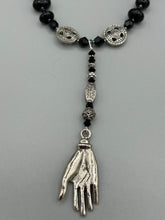 Load image into Gallery viewer, This sophisticated onyx beaded necklace features a large lucky hand charm adorned with floral metal beads, conveying an enchanting aura. The piece is finished with long black glass and floral metal beaded hanging strands, creating a bold and engaging visual statement. Measurements:  Necklace: 19” in length - lucky hand charm is 4” Height
