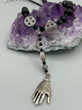 Load image into Gallery viewer, This sophisticated onyx beaded necklace features a large lucky hand charm adorned with floral metal beads, conveying an enchanting aura. The piece is finished with long black glass and floral metal beaded hanging strands, creating a bold and engaging visual statement. Measurements:  Necklace: 19” in length - lucky hand charm is 4” Height
