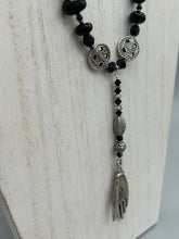 Load image into Gallery viewer, This sophisticated onyx beaded necklace features a large lucky hand charm adorned with floral metal beads, conveying an enchanting aura. The piece is finished with long black glass and floral metal beaded hanging strands, creating a bold and engaging visual statement. Measurements:  Necklace: 19” in length - lucky hand charm is 4” Height
