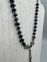 Load image into Gallery viewer, This sophisticated onyx beaded necklace features a large lucky hand charm adorned with floral metal beads, conveying an enchanting aura. The piece is finished with long black glass and floral metal beaded hanging strands, creating a bold and engaging visual statement. Measurements:  Necklace: 19” in length - lucky hand charm is 4” Height
