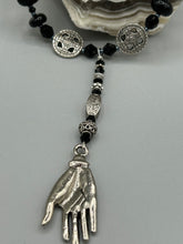 Load image into Gallery viewer, This sophisticated onyx beaded necklace features a large lucky hand charm adorned with floral metal beads, conveying an enchanting aura. The piece is finished with long black glass and floral metal beaded hanging strands, creating a bold and engaging visual statement. Measurements:  Necklace: 19” in length - lucky hand charm is 4” Height
