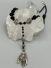 Load image into Gallery viewer, This sophisticated onyx beaded necklace features a large lucky hand charm adorned with floral metal beads, conveying an enchanting aura. The piece is finished with long black glass and floral metal beaded hanging strands, creating a bold and engaging visual statement. Measurements:  Necklace: 19” in length - lucky hand charm is 4” Height
