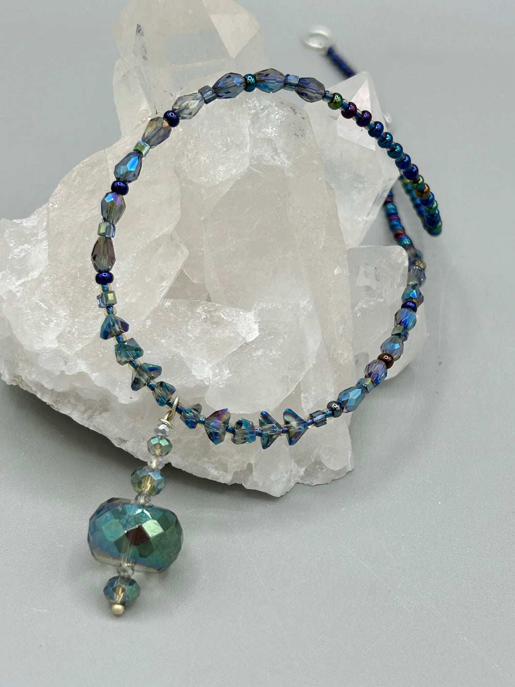 Make a bold statement with this shimmery aqua blue and blue tones glass beaded necklace. The round faceted shaped pendant compliments the cool tones of the necklace, perfect for adding a rich pop of color to any Spring outfit. The draped design gives this piece an elegant, bohemian look.  Measurements:    Necklace is 18” in length, pendant is 1 1/2”