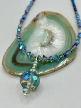 Load image into Gallery viewer, Make a bold statement with this shimmery aqua blue and blue tones glass beaded necklace. The round faceted shaped pendant compliments the cool tones of the necklace, perfect for adding a rich pop of color to any Spring outfit. The draped design gives this piece an elegant, bohemian look.  Measurements:    Necklace is 18” in length, pendant is 1 1/2”
