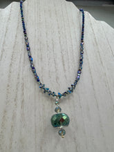 Load image into Gallery viewer, Make a bold statement with this shimmery aqua blue and blue tones glass beaded necklace. The round faceted shaped pendant compliments the cool tones of the necklace, perfect for adding a rich pop of color to any Spring outfit. The draped design gives this piece an elegant, bohemian look.  Measurements:    Necklace is 18” in length, pendant is 1 1/2”
