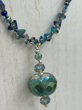 Load image into Gallery viewer, Make a bold statement with this shimmery aqua blue and blue tones glass beaded necklace. The round faceted shaped pendant compliments the cool tones of the necklace, perfect for adding a rich pop of color to any Spring outfit. The draped design gives this piece an elegant, bohemian look.  Measurements:    Necklace is 18” in length, pendant is 1 1/2”
