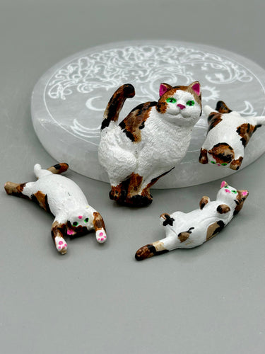 Cat lovers dream, this hand-crafted calico cat magnet art is the purrfect decoration on refrigerators, lockers, cubicles or toolboxes. The set includes one large cat magnet and  three mini cat figurines, featuring emerald green eyes.  Measurements:  H 2” x W 1/2” x D 3/8” - Cat Magnet  H 2” x W 3/8” x D 3/8” -   Cat Figurines