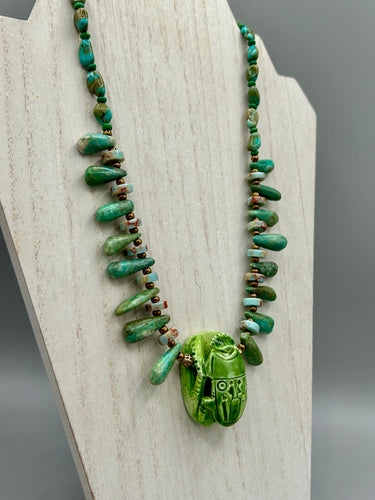 This powerful statement piece necklace features an eye-catching hand sculpted dark blue clay scarab beetle pendant. Adorned with green magnesite and serpentine teintee stone beaded necklace, this dramatic necklace artfully wraps around the neck, conveying an elegant and bold style. Necklace is 20 1/4