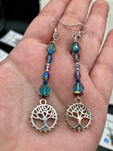 Load image into Gallery viewer, This captivating set of earrings boasts an exquisite range of intense blues and purples, accented with a warm touch of gold and green. The dangling silver plated tree of life charm adds a beautiful finishing touch.  Measurements: 2 1/2” in length
