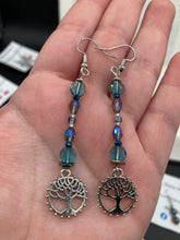 Load image into Gallery viewer, This captivating set of earrings boasts an exquisite range of intense blues and purples, accented with a warm touch of gold and green. The dangling silver plated tree of life charm adds a beautiful finishing touch.  Measurements: 2 1/2” in length
