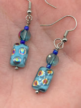 Load image into Gallery viewer, This set of glass beaded earrings features a vibrant blue shade with hints of purples and gold for an overall dynamic look. Its unique texture is derived from the combination of different size and shaped beads, resulting in a bold, eye-catching piece. For any discerning connoisseur, this set is a must-have addition to any jewelry collection.  Measurements: 1 1/2” in length
