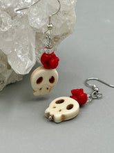 Load image into Gallery viewer, These stylish skull earrings are perfect for adding a unique flair to any outfit. Whether you&#39;re looking for a Dia De Los Muertos accessory or simply looking to draw inspiration, these goth pieces perfectly capture the vampire goth, witchy, dark, Chingona Cabrona, Latina Chicana styles. Howlite stone skull bead with red quartzize floral beads.  Measurements: 1 1/4 ” in length
