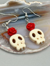 Load image into Gallery viewer, These stylish skull earrings are perfect for adding a unique flair to any outfit. Whether you&#39;re looking for a Dia De Los Muertos accessory or simply looking to draw inspiration, these goth pieces perfectly capture the vampire goth, witchy, dark, Chingona Cabrona, Latina Chicana styles. Howlite stone skull bead with red quartzize floral beads.  Measurements: 1 1/4 ” in length
