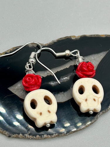 These stylish skull earrings are perfect for adding a unique flair to any outfit. Whether you're looking for a Dia De Los Muertos accessory or simply looking to draw inspiration, these goth pieces perfectly capture the vampire goth, witchy, dark, Chingona Cabrona, Latina Chicana styles. Howlite stone skull bead with red quartzize floral beads.  Measurements: 1 1/4 ” in length