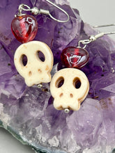 Load image into Gallery viewer, These stylish skull earrings are perfect for adding a unique flair to any outfit. Whether you&#39;re looking for a Dia De Los Muertos accessory or simply looking to draw inspiration, these goth pieces perfectly capture the vampire goth, witchy, dark, Chingona Cabrona, Latina Chicana styles. Howlite stone skull beaded earrings come with a ruby red heart-shaped glass beaded that has a very shimmery and vivid iridescent hue.  Measurements: 1 1/4 ” in length
