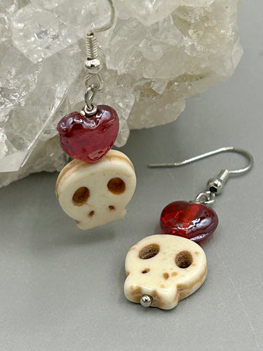 These stylish skull earrings are perfect for adding a unique flair to any outfit. Whether you're looking for a Dia De Los Muertos accessory or simply looking to draw inspiration, these goth pieces perfectly capture the vampire goth, witchy, dark, Chingona Cabrona, Latina Chicana styles. Howlite stone skull beaded earrings come with a ruby red heart-shaped glass beaded that has a very shimmery and vivid iridescent hue.  Measurements: 1 1/4 ” in length