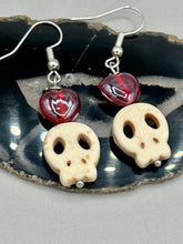 Load image into Gallery viewer, These stylish skull earrings are perfect for adding a unique flair to any outfit. Whether you&#39;re looking for a Dia De Los Muertos accessory or simply looking to draw inspiration, these goth pieces perfectly capture the vampire goth, witchy, dark, Chingona Cabrona, Latina Chicana styles. Howlite stone skull beaded earrings come with a ruby red heart-shaped glass beaded that has a very shimmery and vivid iridescent hue.  Measurements: 1 1/4 ” in length
