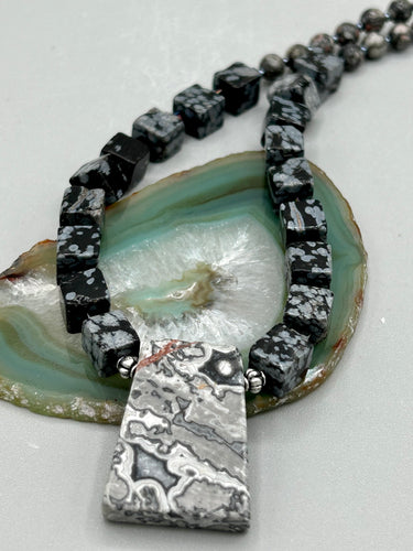 This rustic necklace features an eye-catching large trapezoid-shaped Picasso jasper, hematite, square-shaped snowflake obsidian combo set in a unique and chic design. Handcrafted from genuine stones, this necklace is perfect for any bohemian look.   Measurements:  Necklace is 21