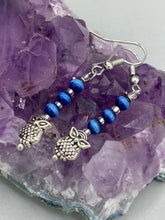 Load image into Gallery viewer, Chic and fun silver-plated owl charm earrings featuring delicate dark blue cats eye beads. Measurements: 1 3/16” in length
